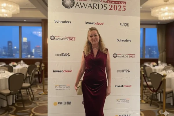 Wealth Briefing Asia Awards 2025, Woman in a burgundy velvet evening gown standing in front of a WealthBriefingAsia Awards 2025 step-and-repeat banner at a formal event venue.
